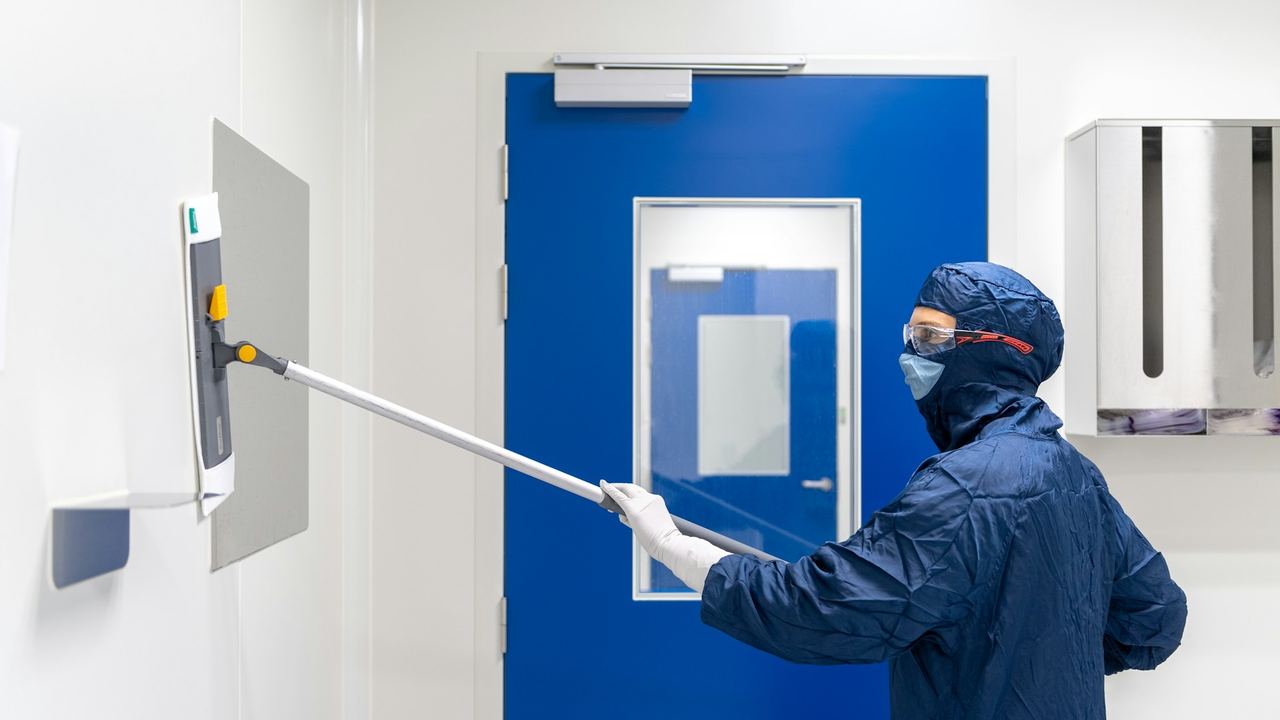 Technicien en combinaison de protection intégrale nettoyant une paroi dans un local professionnel