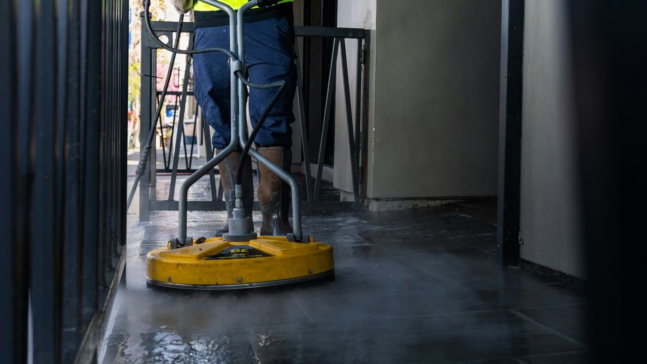 Technicien nettoyant un sol au monobrosse haute pression, vapeur au ras du sol