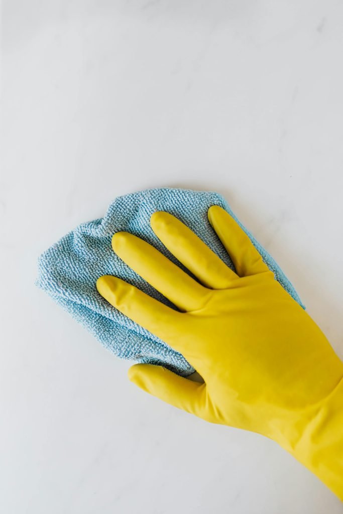 Yellow gloved hand wiping surface with blue cloth, concept of cleaning and hygiene.